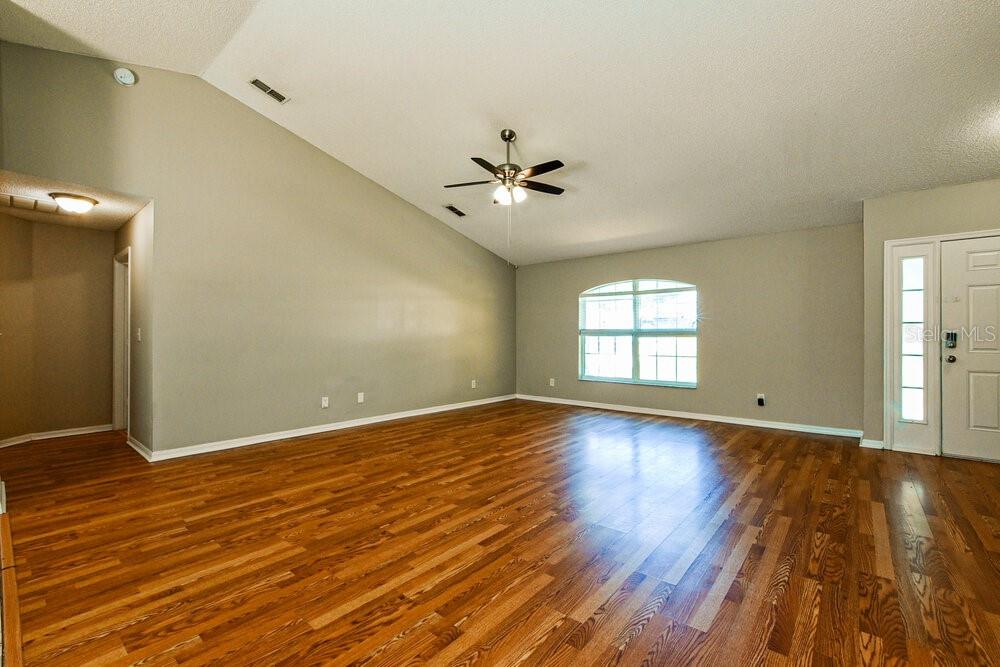 An empty living room features vaulted ceilings, a ceiling fan, and hardwood flooring — 1320 RAIN FOREST LANE, MINNEOLA, FL