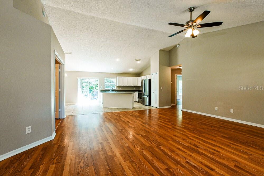 A living room with hardwood floors leads to an open kitchen with white cabinets — 1320 RAIN FOREST LANE, MINNEOLA, FL