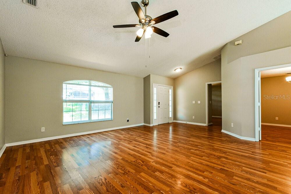 An empty living room features wood-look flooring, a ceiling fan, and a large arched window — 1320 RAIN FOREST LANE, MINNEOLA, FL
