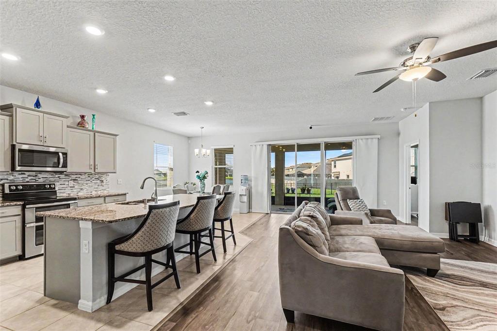 A kitchen with granite countertops, stainless steel appliances, and light cabinetry opens to a dining area — 16639 GOOSE RIBBON PLACE, WIMAUMA, FL
