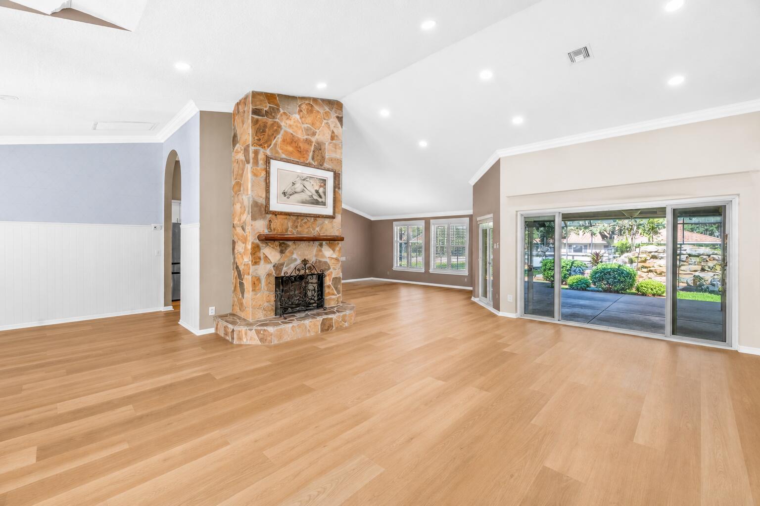 A spacious living room features light wood flooring, a stone fireplace, and large sliding glass doors — 2559 Palm Deer Drive, Loxahatchee FL 33470, LOXAHATCHEE, FL