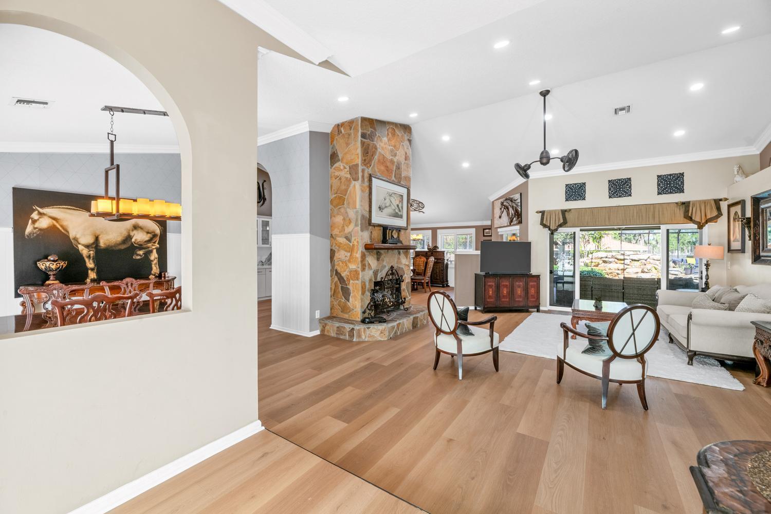A living room features a stone fireplace, light wood flooring, and an arched entryway — 2559 Palm Deer Drive, Loxahatchee FL 33470, LOXAHATCHEE, FL