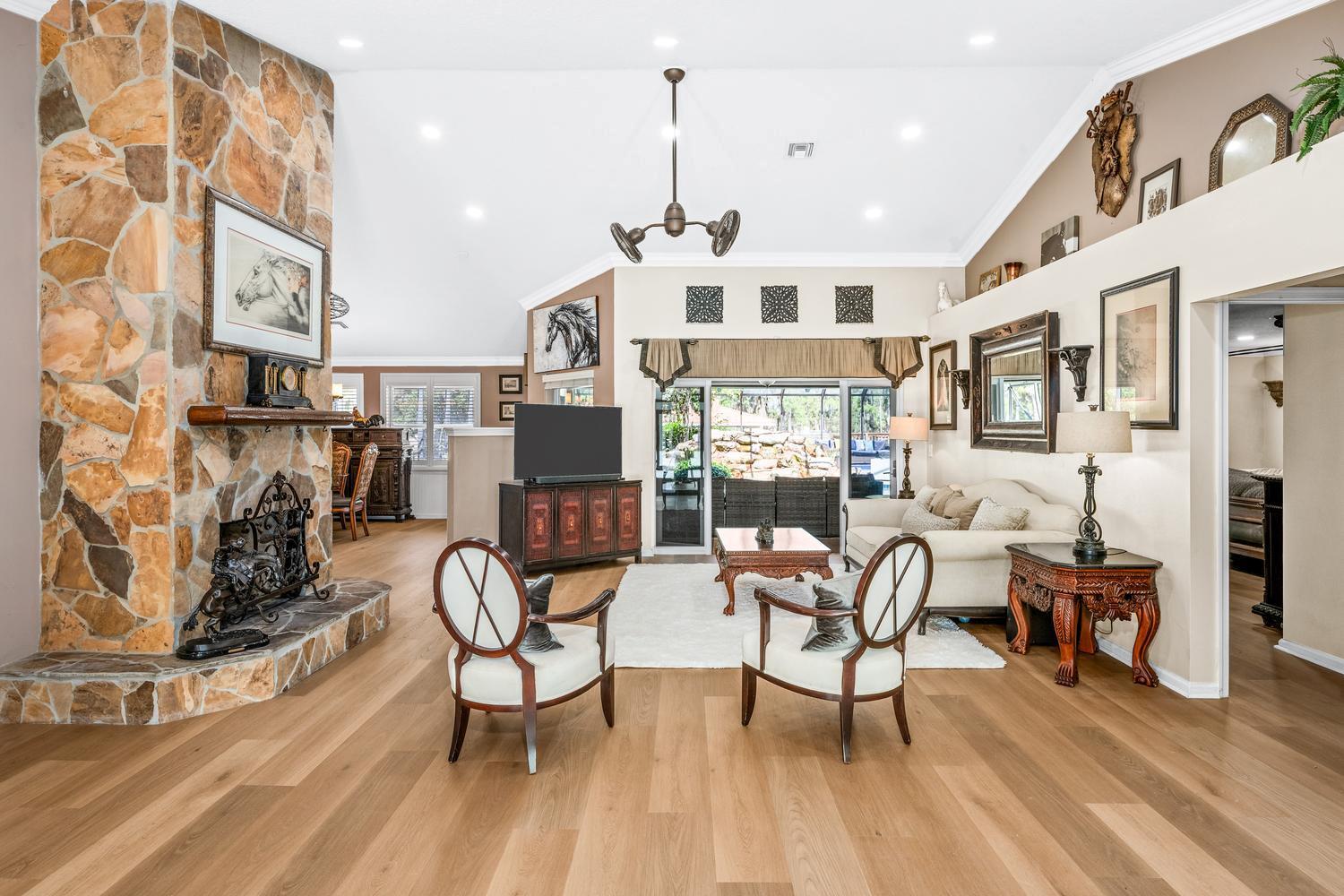 A living room features a stone fireplace, vaulted ceilings, hardwood floors, and a sliding glass door — 2559 Palm Deer Drive, Loxahatchee FL 33470, LOXAHATCHEE, FL