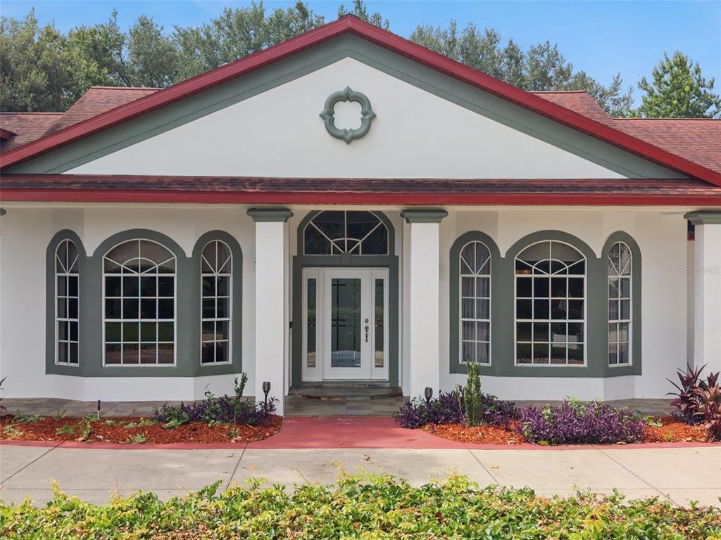 The front exterior of a white house features a red roof, arched windows, and columns — 15000 THOROUGHBRED LN, MONTVERDE, FL
