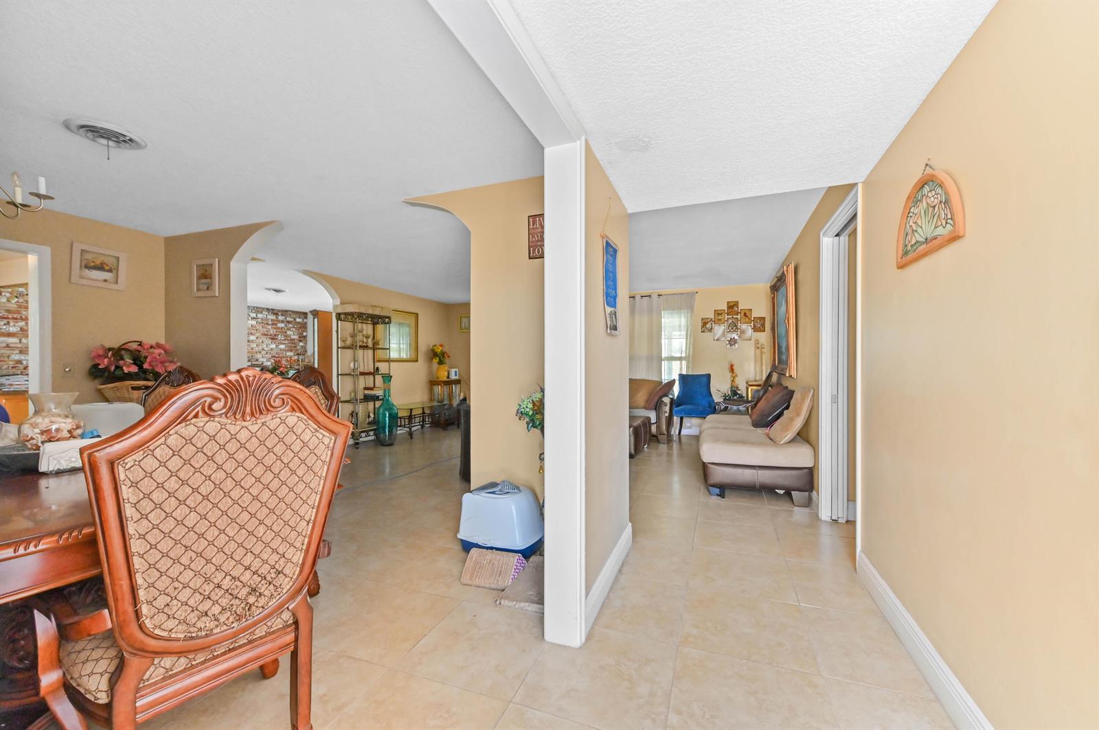 A dining area with a wooden chair leads into a living room with tiled floors — 315 SW 12th Avenue, Boynton Beach FL 33435, BOYNTON BEACH, FL