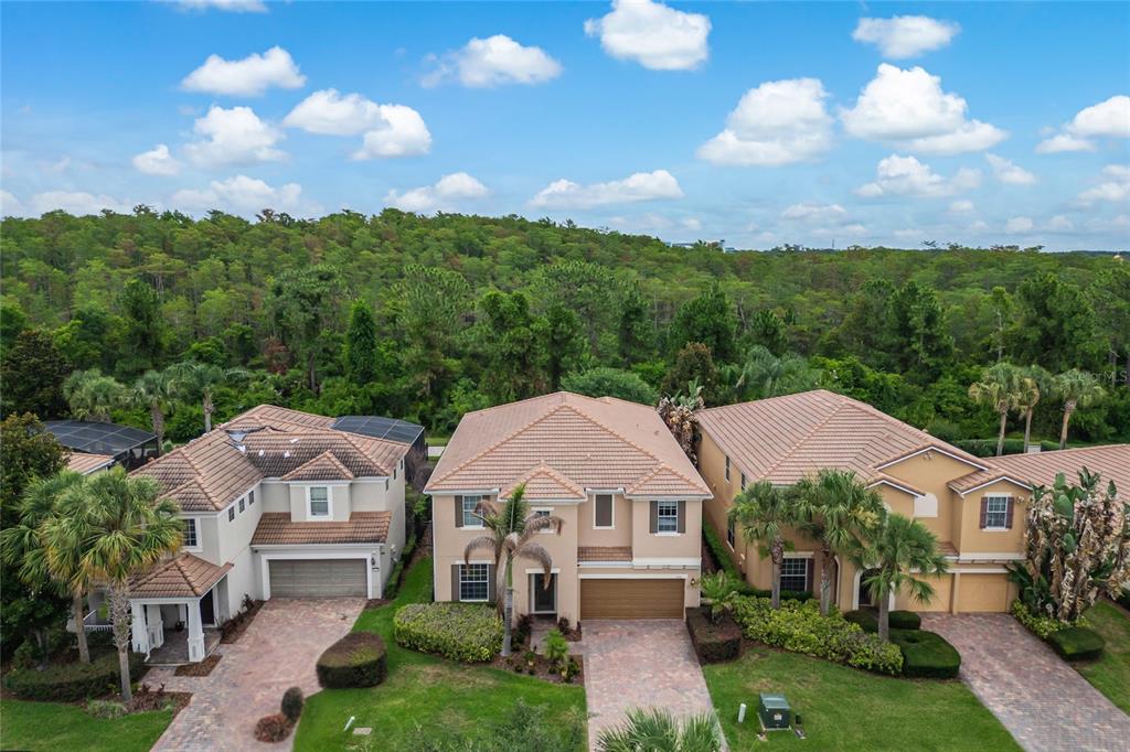 An aerial view shows three suburban houses with tiled roofs and paved driveways near woods — 11763 AURELIO LN, ORLANDO, FL