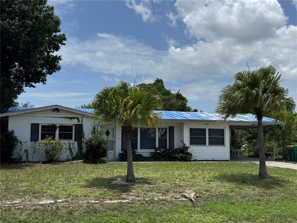 A single-story white house features a blue metal roof, two palm trees, and a carport — 27233 WHITMAN AVENUE, PUNTA GORDA, FL