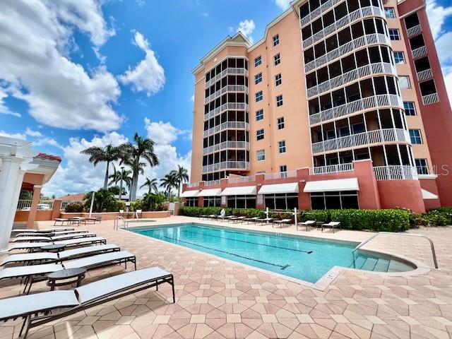 A multi-story peach-colored building stands beside a rectangular swimming pool with lounge chairs on deck — 3191 MATECUMBE KEY ROAD UNIT 206, PUNTA GORDA, FL