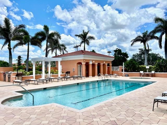 A swimming pool with a pergola and clubhouse sits on a paved patio with palm trees — 3191 MATECUMBE KEY ROAD UNIT 206, PUNTA GORDA, FL