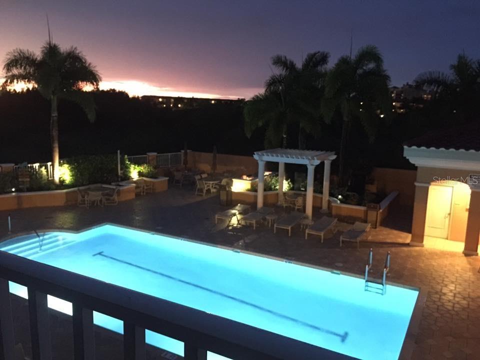 An illuminated swimming pool sits on a patio with lounge chairs and palm trees at dusk — 3191 MATECUMBE KEY ROAD UNIT 206, PUNTA GORDA, FL
