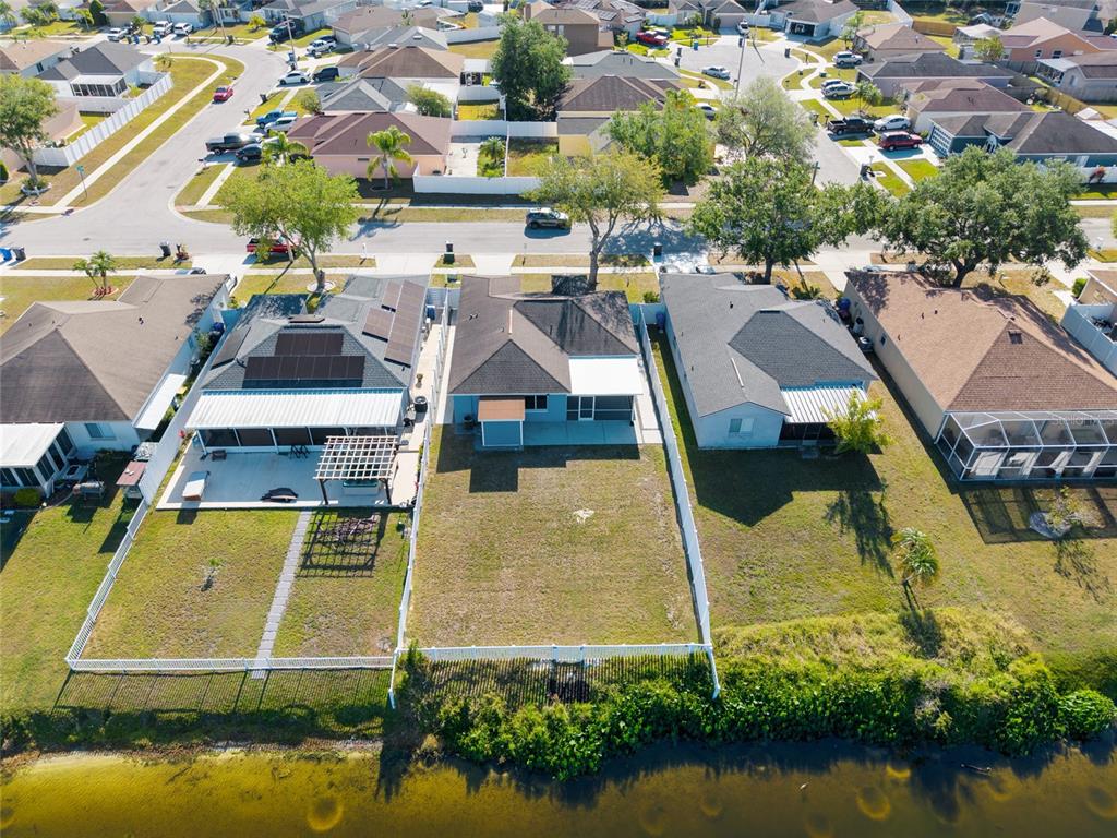 An aerial view shows three suburban houses with fenced backyards bordering a small lake — 1305 FLEXFORD STREET, BRANDON, FL
