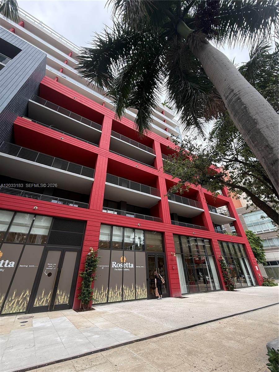 A low-angle exterior view of a modern building with red balconies and a ground-floor bakery — 90 NE 32 street # 623, Miami FL 33127, MIAMI, FL