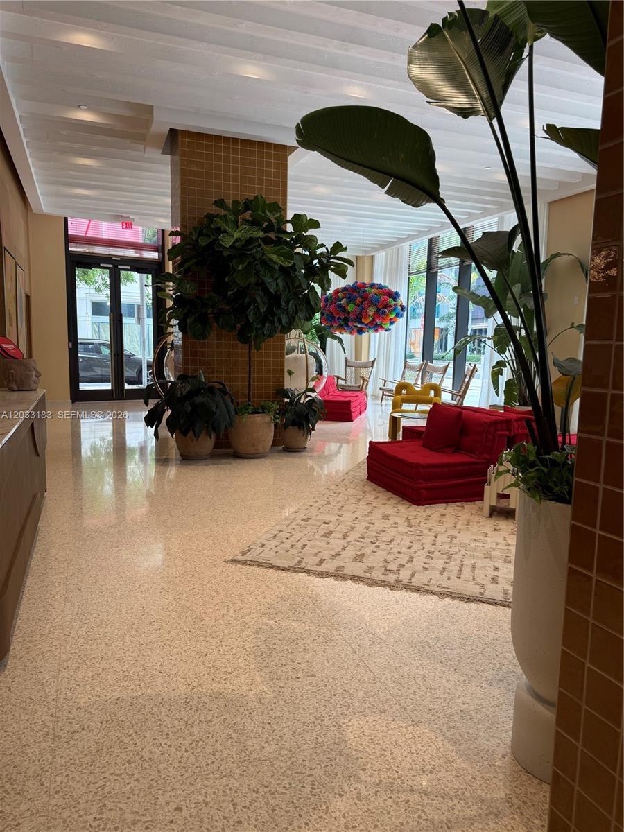 A modern lobby features a tiled pillar, potted plants, red seating, and a colorful light fixture — 90 NE 32 street # 623, Miami FL 33127, MIAMI, FL