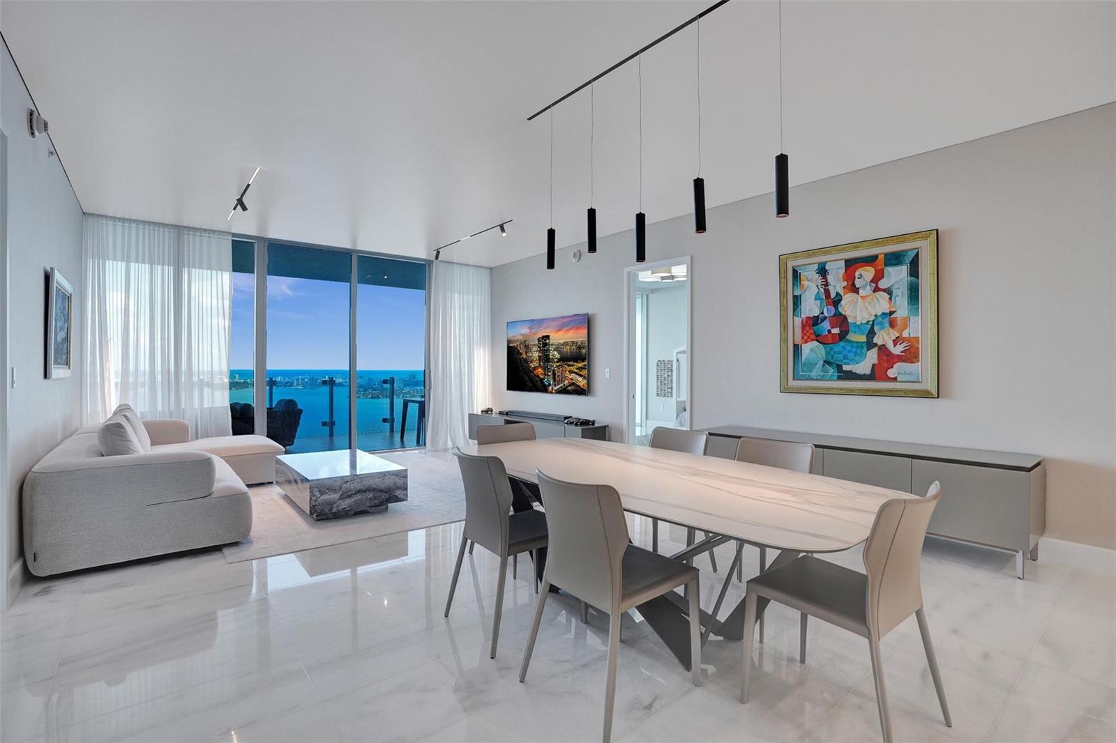 A modern dining and living area features a marble table, white floors, and ocean views — 700 NE 26th Terrace # 4702, Miami FL 33137, MIAMI, FL