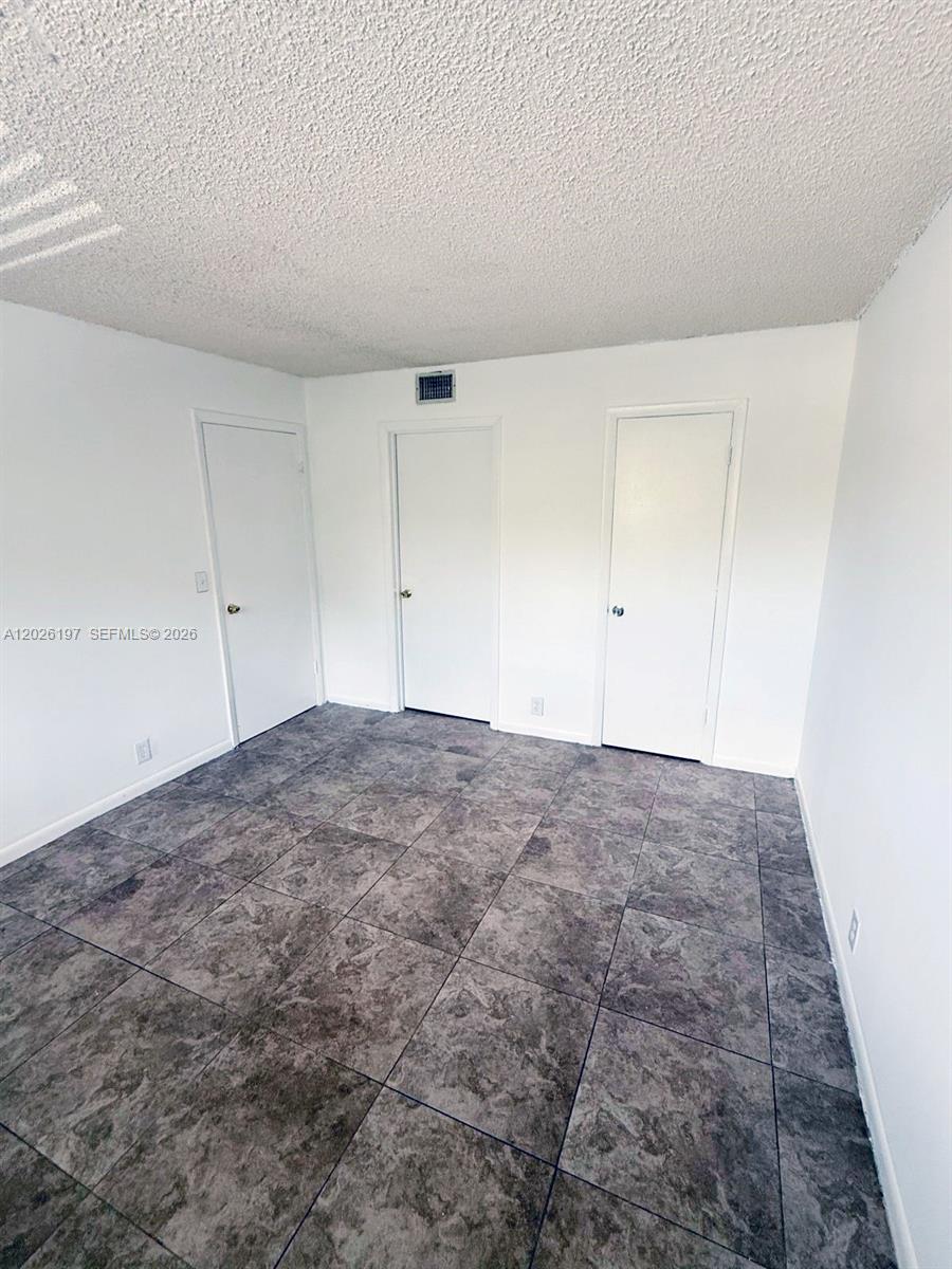 An empty room features white walls, a textured ceiling, and dark gray tiled flooring — 2070 NW 43rd Ter # 6, Lauderhill FL 33313, LAUDERHILL, FL