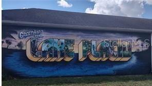A large mural on the side of a building displays the words Greetings from Lake Placid — 455 NICHELE BOULEVARD, LAKE PLACID, FL