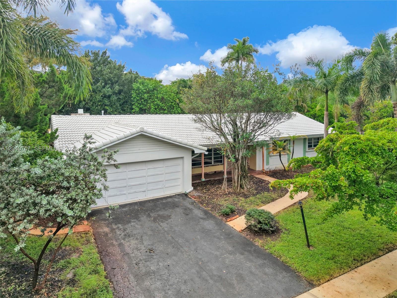An exterior view of a single-story house with a white tile roof and attached garage — 600 Petunia Dr, Plantation FL 33317, PLANTATION, FL