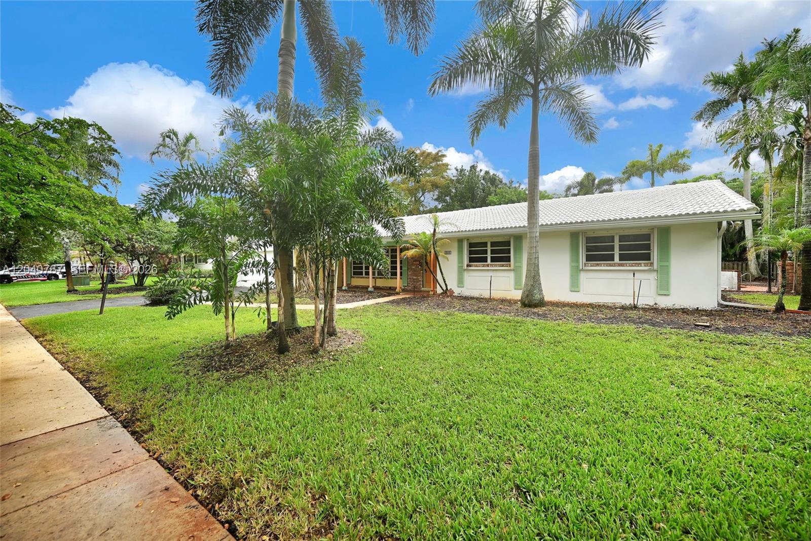A single-story white house with a tiled roof sits behind a green lawn and palms — 600 Petunia Dr, Plantation FL 33317, PLANTATION, FL