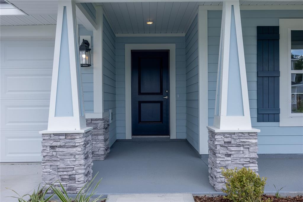 A covered front porch features light blue siding, stone-based columns, and a dark blue door — 2602 SW 250TH TERRACE, NEWBERRY, FL