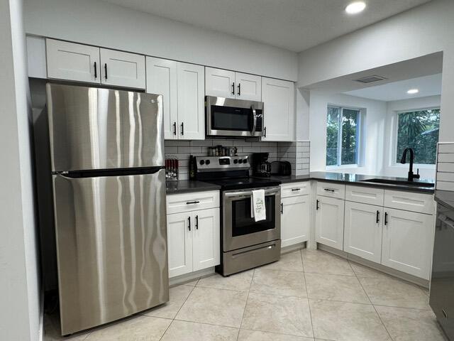 A kitchen features white cabinets, stainless steel appliances, dark countertops, and a tile backsplash — 1632 NW 5th Street, Boca Raton FL 33486, BOCA RATON, FL