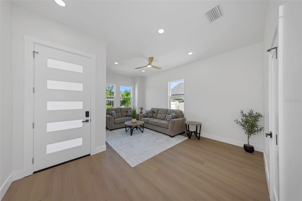 A bright living room features light wood flooring, a white front door, and gray sofas — 617 FOLSOM STREET S, ST PETERSBURG, FL