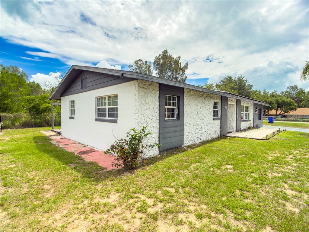 A single-story house with white stone walls, gray trim, and a gabled roof — 4420 AVISTA STREET, SEBRING, FL