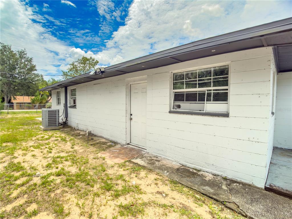 The exterior of a white concrete block house features a door, window, and air conditioner — 4420 AVISTA STREET, SEBRING, FL
