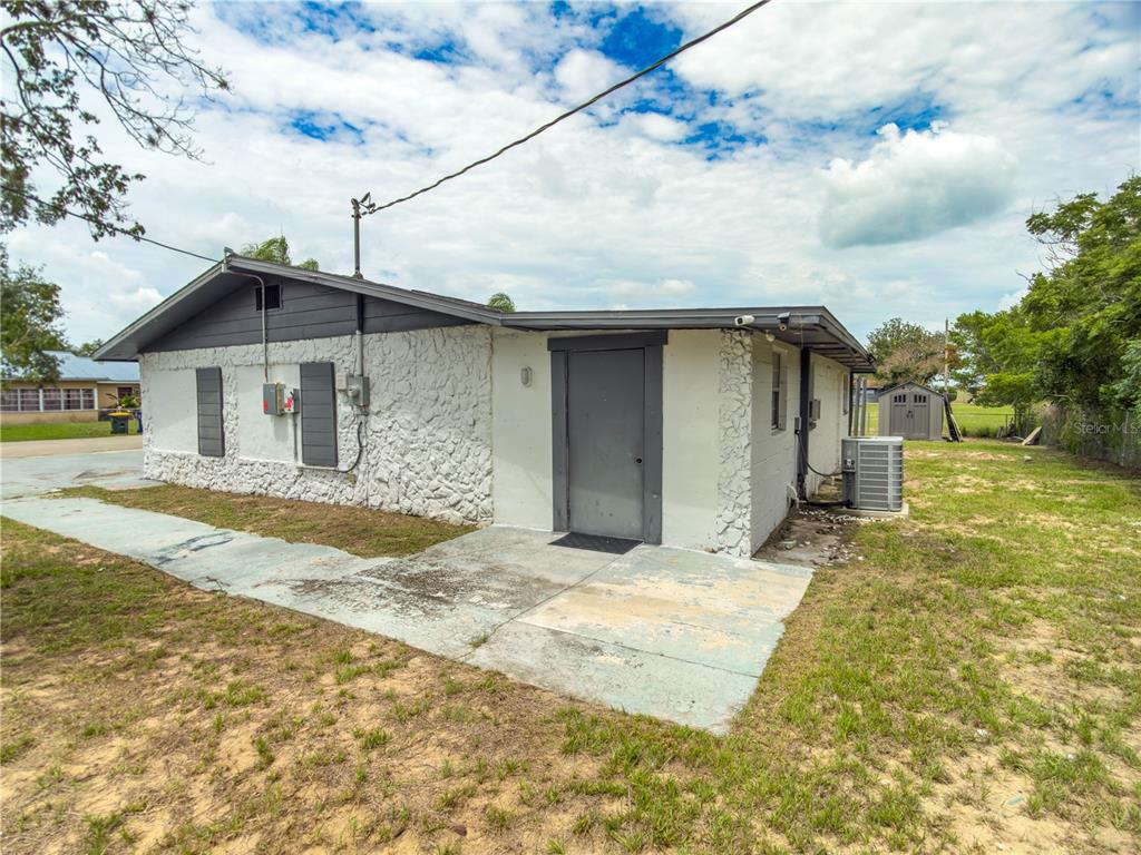 The exterior of a white, stone-textured house features a gray door and a concrete patio — 4420 AVISTA STREET, SEBRING, FL