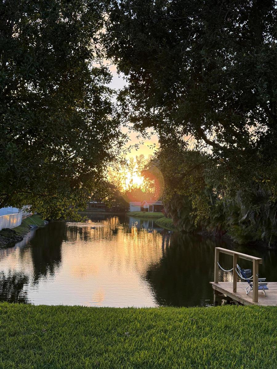 A sunset view over a backyard pond with a wooden dock and surrounding trees — 1417 Willow Road, West Palm Beach FL 33406, WEST PALM BEACH, FL