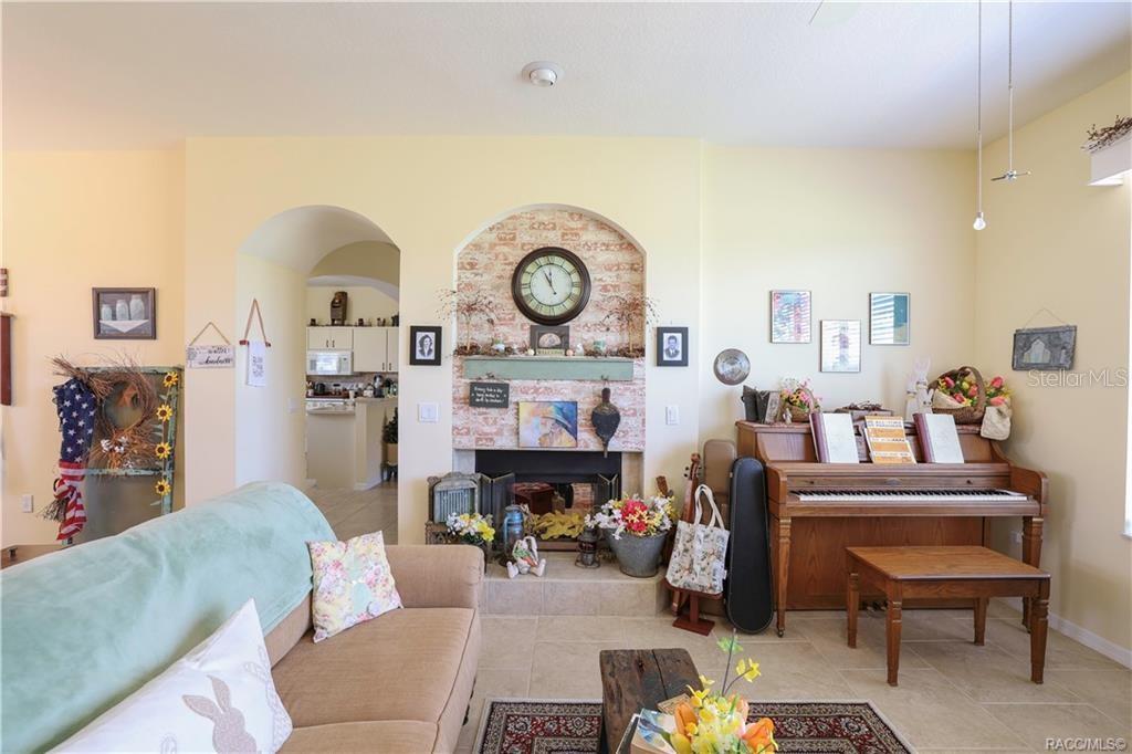 A living room features a brick fireplace, a piano, and an arched entryway to the kitchen — 209 W REXFORD DRIVE, BEVERLY HILLS, FL