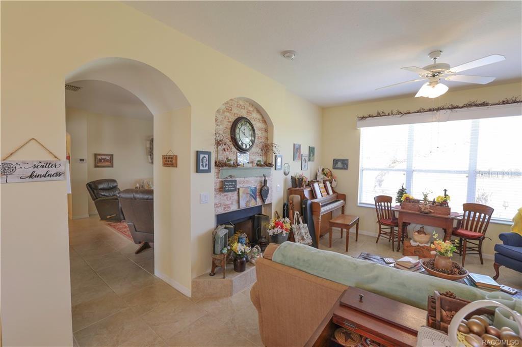 A living room features a fireplace with a brick arch, a piano, and tile flooring — 209 W REXFORD DRIVE, BEVERLY HILLS, FL
