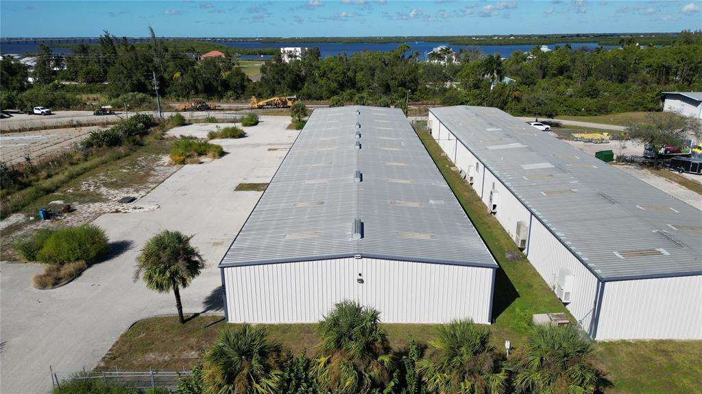 An aerial view shows two long, metal-roofed industrial warehouse buildings surrounded by paved lots and vegetation — 5469 WILLIAMSBURG DRIVE, PUNTA GORDA, FL