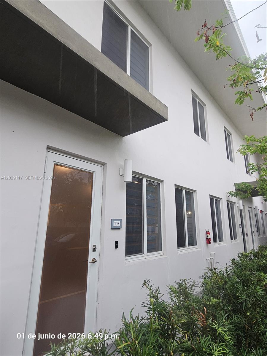 The exterior of a modern white two-story building features a glass-paneled front door labeled 103 — 6453 NW 102nd Path # 103, Doral FL 33178, DORAL, FL