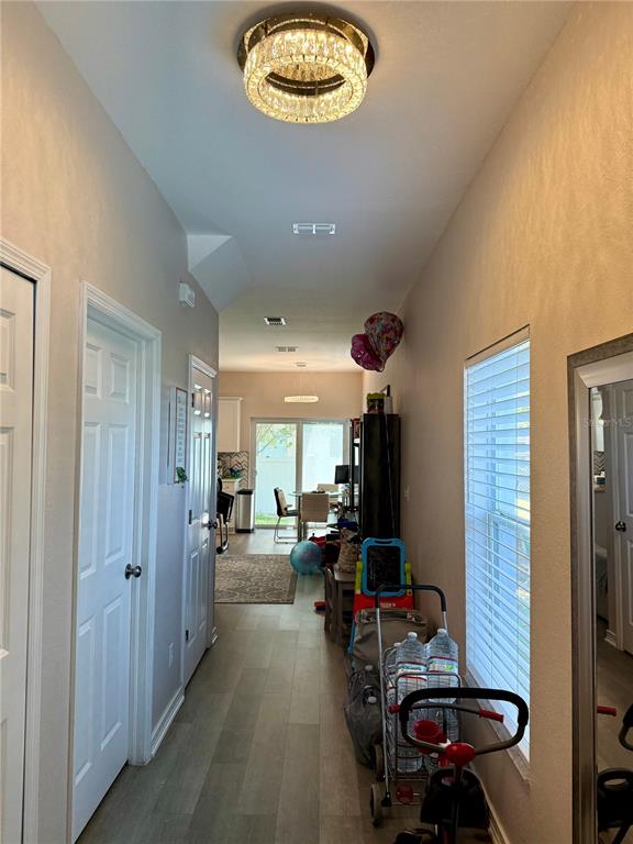 A hallway with light wood-look flooring leads to a dining area and a living space — 13201 OPAL COURT, LARGO, FL