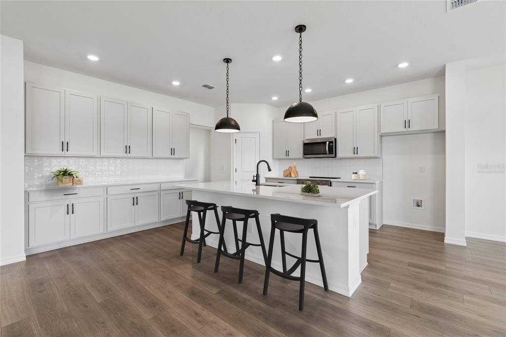 A modern kitchen features white cabinetry, a central island, stainless steel appliances, and wood flooring — 622 KINGSWOOD COURT, BRADENTON, FL