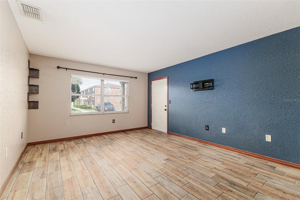 A living room features wood-look tile flooring, a blue accent wall, and a single window — 1920 E EDGEWOOD DRIVE UNIT R3, LAKELAND, FL