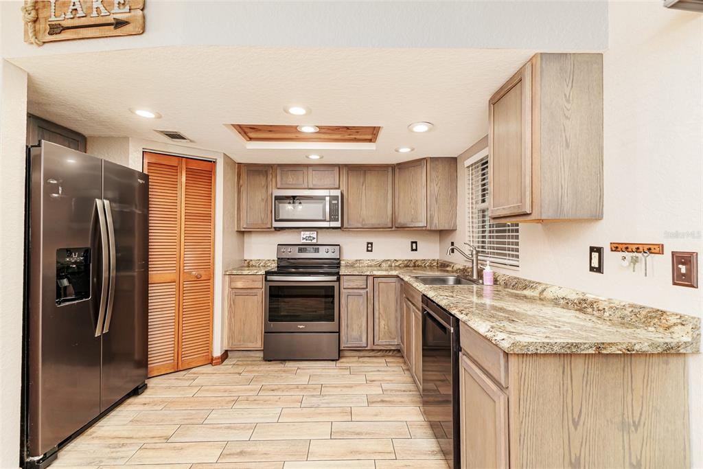 A kitchen features wood cabinets, granite countertops, stainless steel appliances, and light-colored tile flooring — 1920 E EDGEWOOD DRIVE UNIT R3, LAKELAND, FL