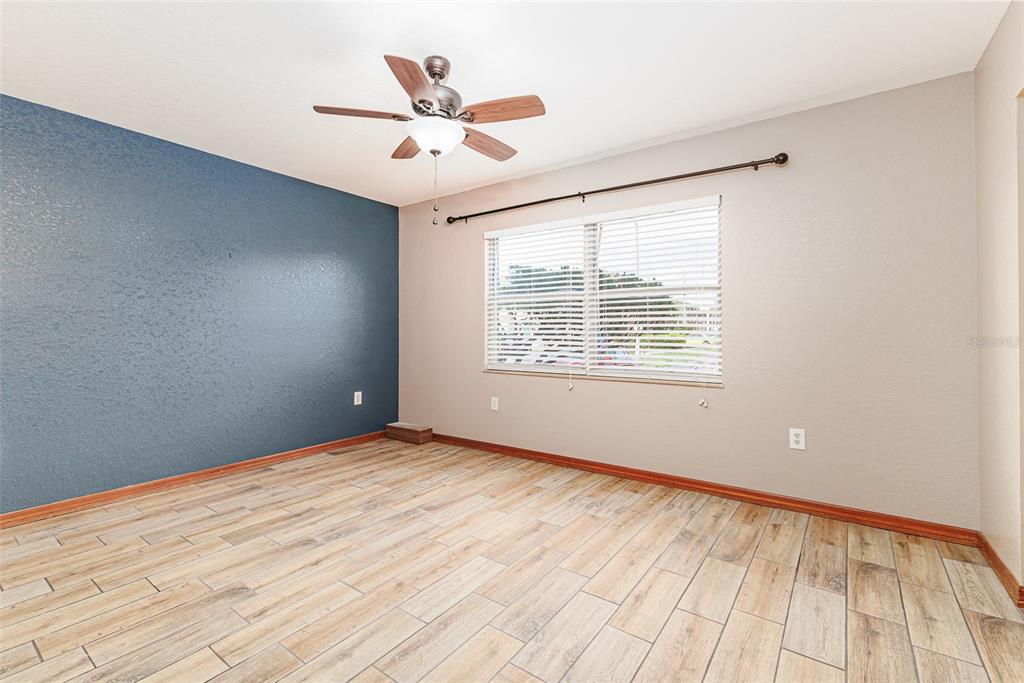 An empty bedroom features wood-look tile flooring, a blue accent wall, and a ceiling fan — 1920 E EDGEWOOD DRIVE UNIT R3, LAKELAND, FL