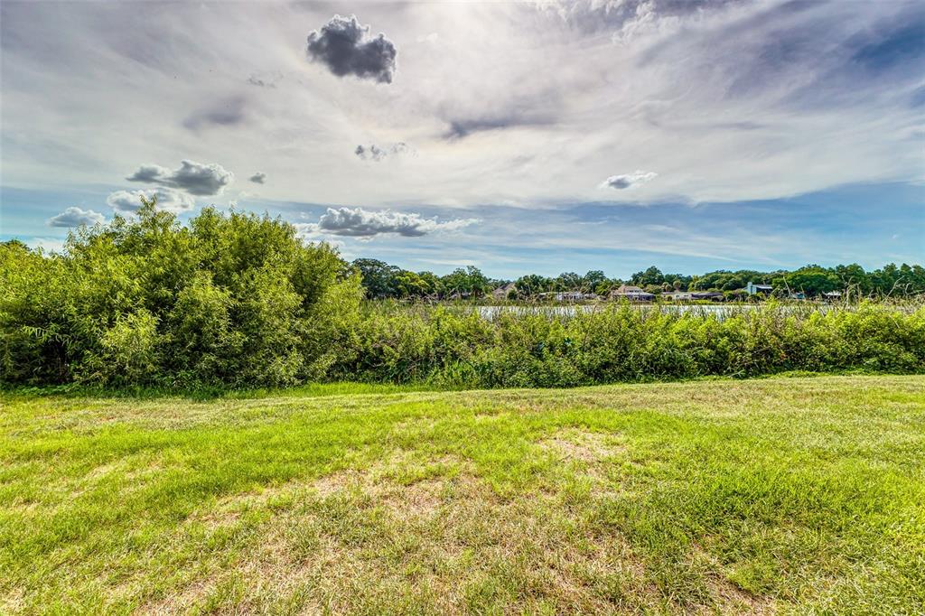A grassy lawn overlooks a dense line of bushes and trees bordering a distant lake — 1920 E EDGEWOOD DRIVE UNIT R3, LAKELAND, FL
