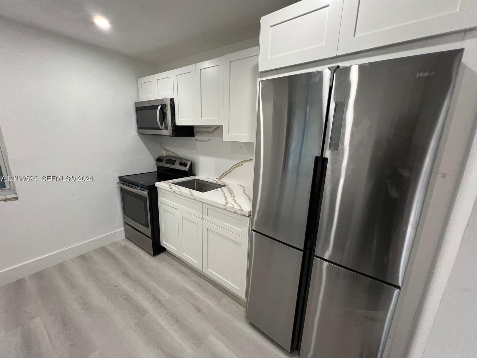 A kitchen features white cabinets, stainless steel appliances, and marble-patterned countertops — 428 NW 97th St # 0, Miami FL 33150, MIAMI, FL