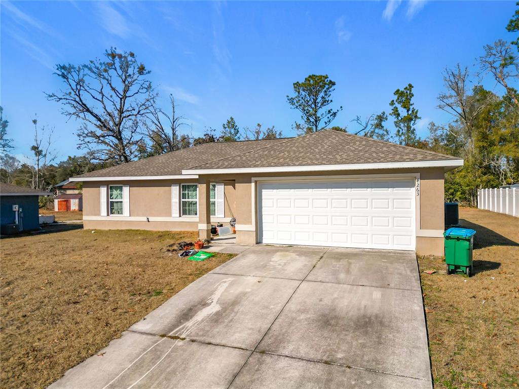 A single-story house with a tan exterior, a white garage door, and a concrete driveway — 4263 SW 139TH PLACE, OCALA, FL