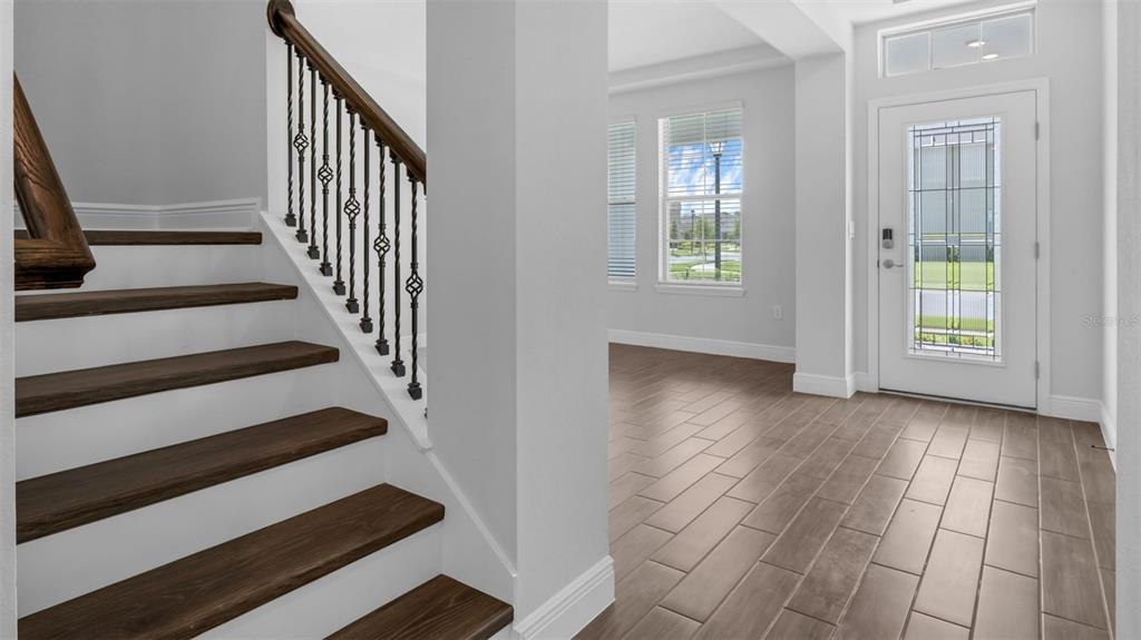 An entryway features a wooden staircase with iron railings and light-colored tile flooring — 11905 SHINE VIEW LANE, WINTER GARDEN, FL