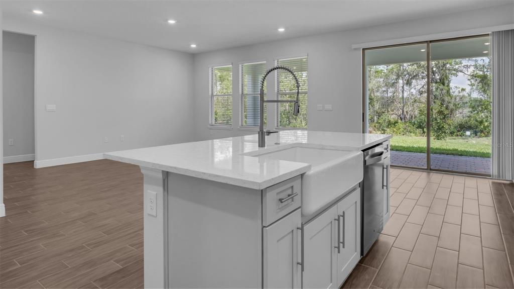 A kitchen island with a farmhouse sink and quartz countertop sits in a modern open-concept room — 11905 SHINE VIEW LANE, WINTER GARDEN, FL