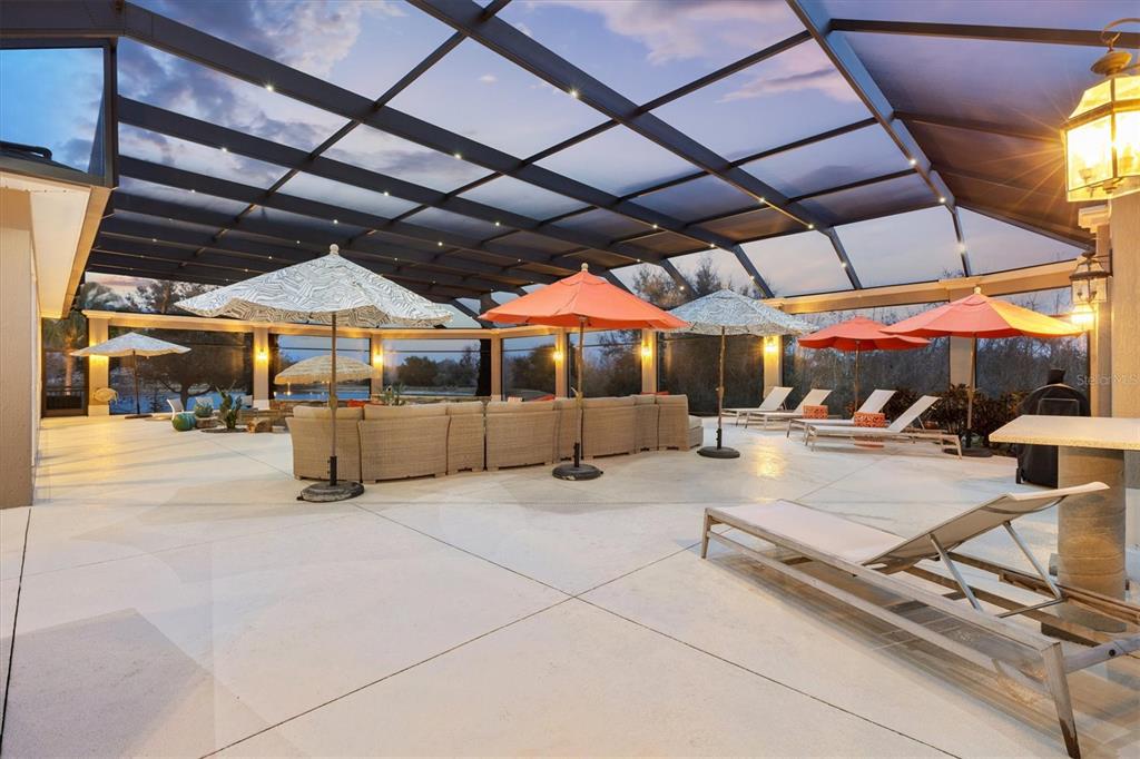 A large screened-in patio features a sectional sofa, lounge chairs, and multiple umbrellas — 885 IRON OAK WAY, THE VILLAGES, FL