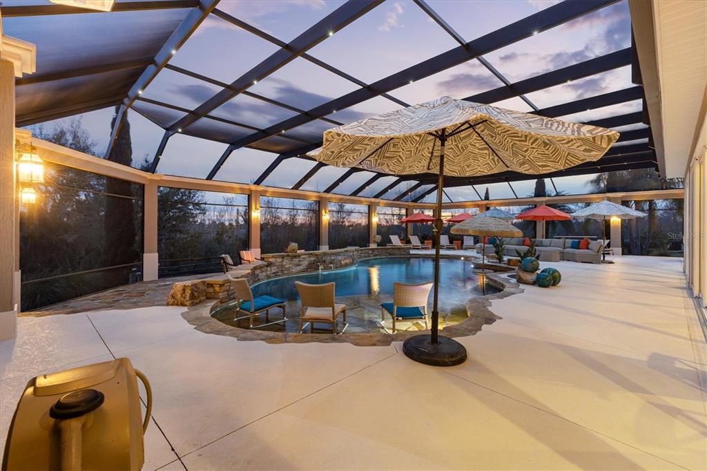A screened-in patio features a swimming pool with stone accents, lounge chairs, and patio umbrellas — 885 IRON OAK WAY, THE VILLAGES, FL