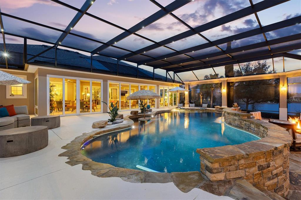 A screened-in patio features a stone-accented swimming pool with a waterfall and outdoor seating — 885 IRON OAK WAY, THE VILLAGES, FL