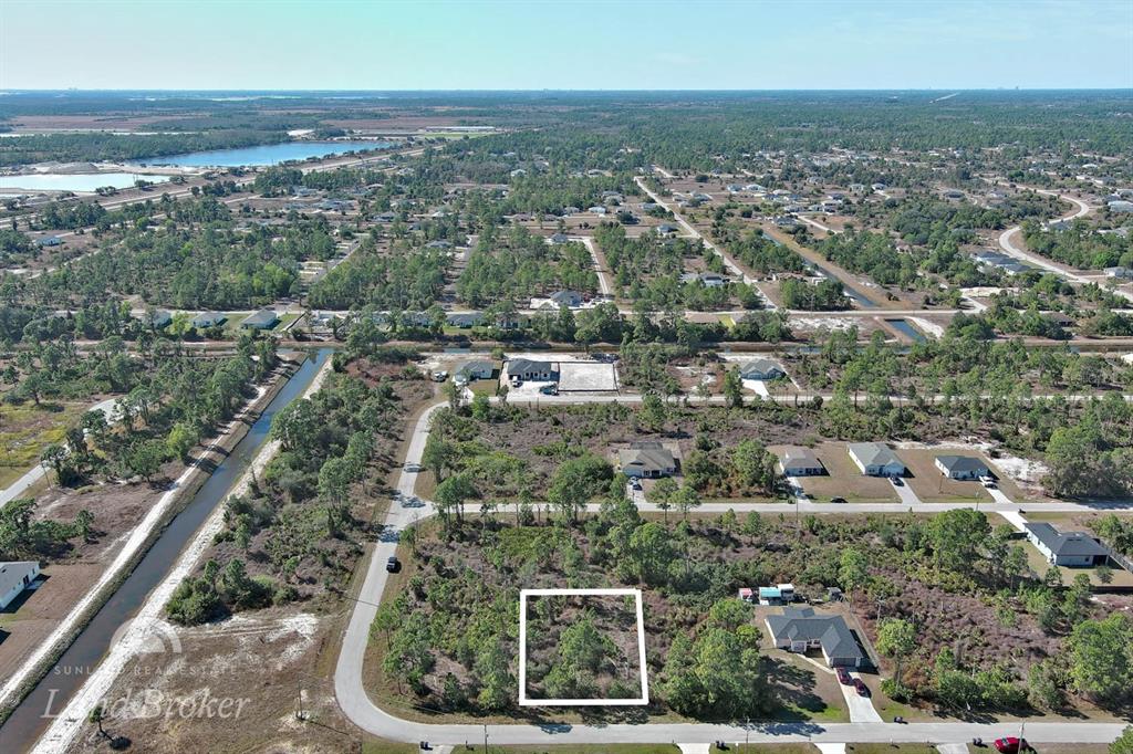 An aerial view shows a vacant, wooded residential lot outlined in white within a neighborhood — 1053 FAYETTE AVENUE, LEHIGH ACRES, FL