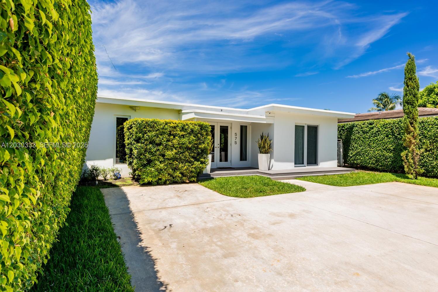 A white single-story house features a concrete driveway, manicured hedges, and a flat roof — 575 W 50th St, Miami Beach FL 33140, MIAMI BEACH, FL