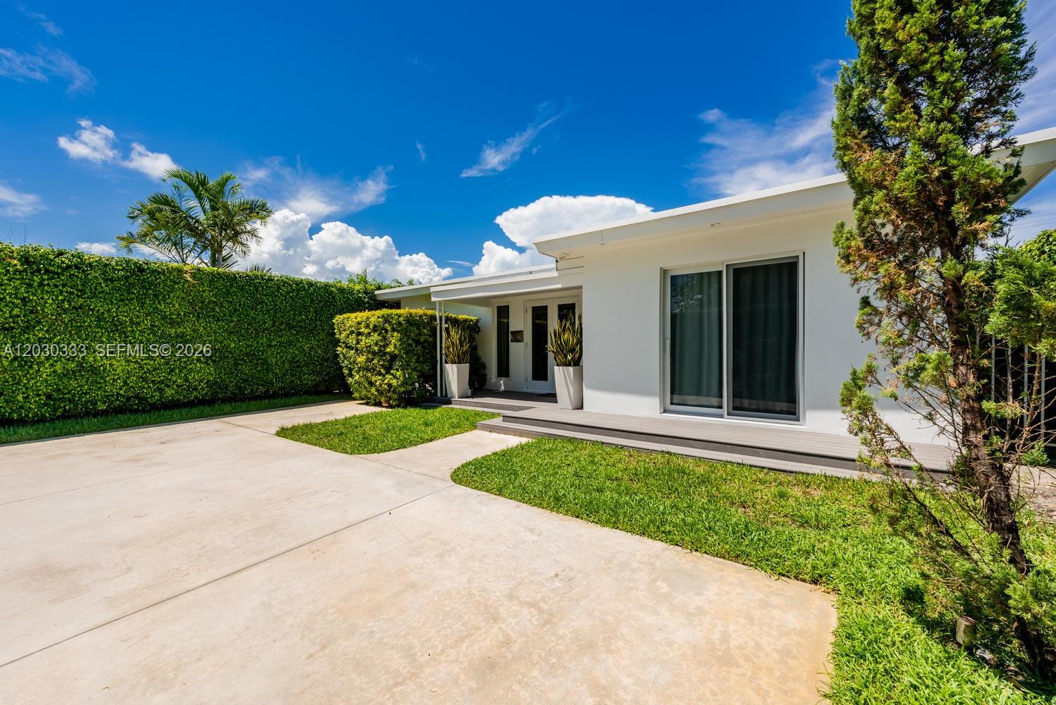 A white single-story house features a concrete driveway, a green hedge, and a wooden deck — 575 W 50th St, Miami Beach FL 33140, MIAMI BEACH, FL