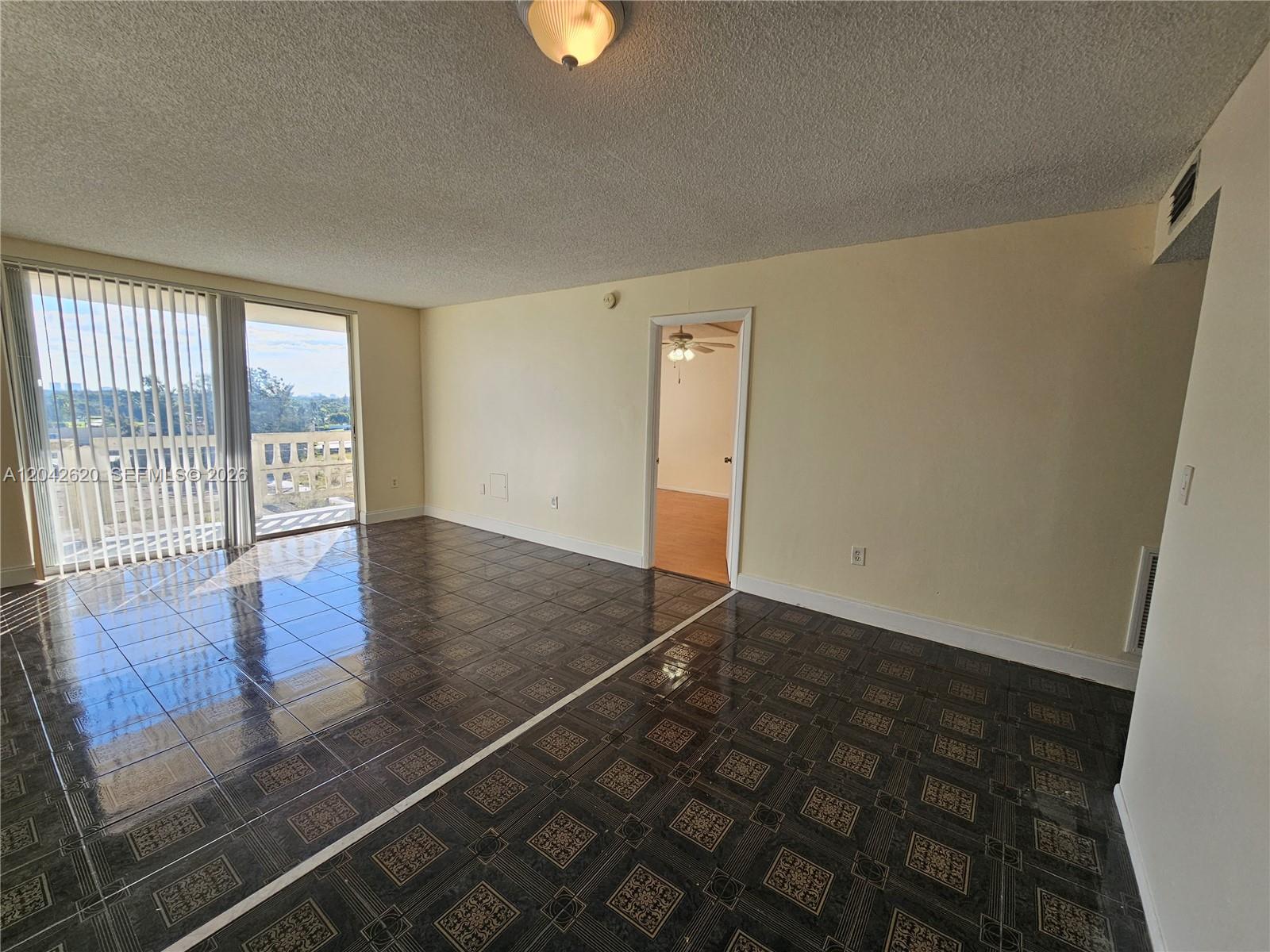 An empty room features dark patterned tile flooring, light-colored walls, and a sliding glass door — 15600 NW 7th Ave # 704, Miami FL 33169, MIAMI, FL